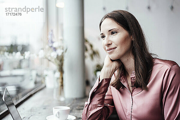 Weibliche Unternehmerin schaut mit der Hand am Kinn in einem Café weg