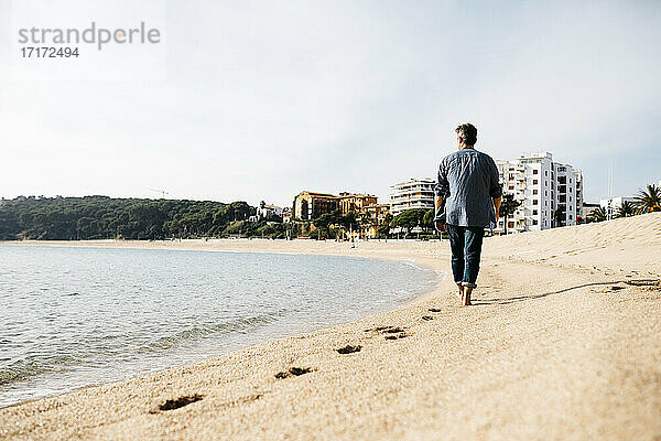 Mann spaziert am Strand an einem sonnigen Tag