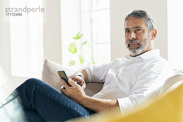 Geschäftsmann mit Smartphone schaut weg  während er zu Hause sitzt