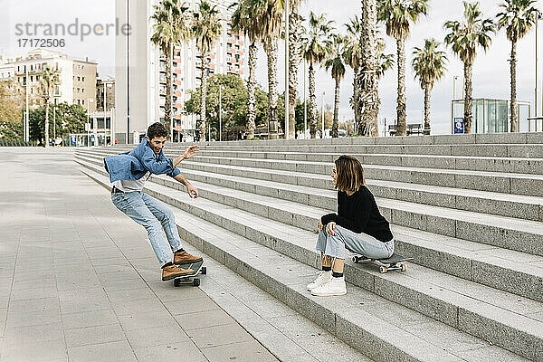 Junge Frau  die auf einer Treppe sitzt und einem Mann beim Skateboarden zusieht