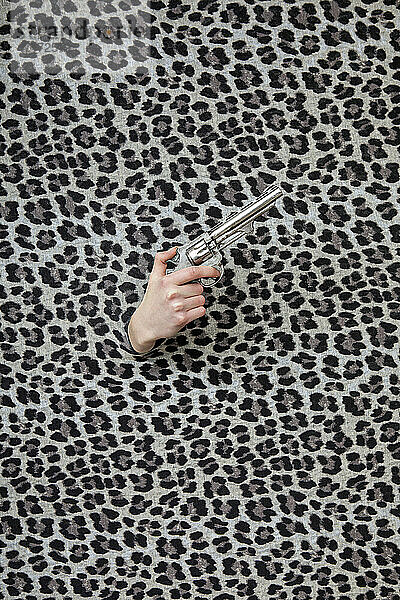 Studio shot of female hand holding old-fashioned revolver through leopard print pattern