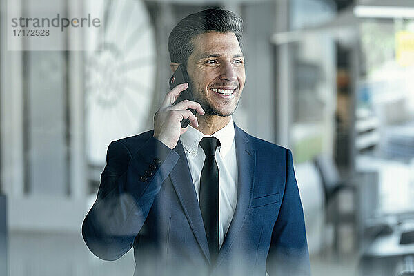 Unternehmerin lächelt  während sie im Büro steht und mit dem Handy spricht