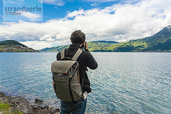 Männlicher Tourist mit Rucksack fotografiert den Sarner See gegen den bewölkten Himmel in der Schweiz