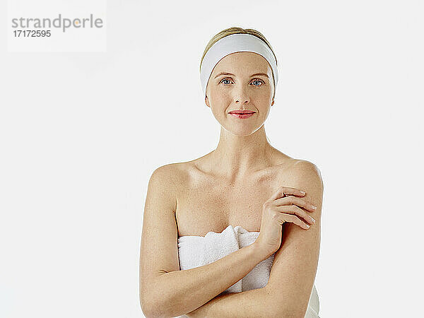 Young woman with headband wrapped in towel staring while standing against white background