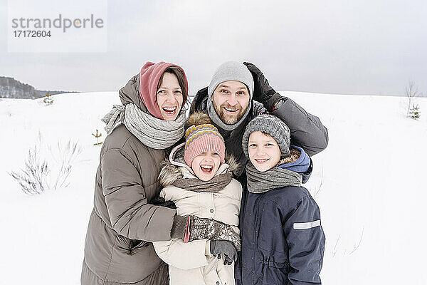 Glückliche Familie auf schneebedecktem Land gegen den Himmel im Urlaub stehend
