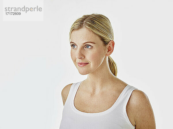 Young woman looking away while standing against white background