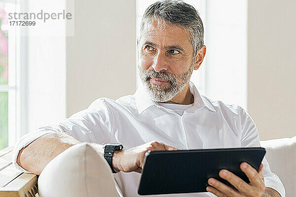 Geschäftsmann mit digitalem Tablet  der wegschaut  während er zu Hause sitzt