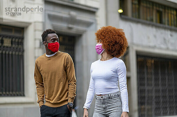 Couple wearing face mask looking at each other while walking in city