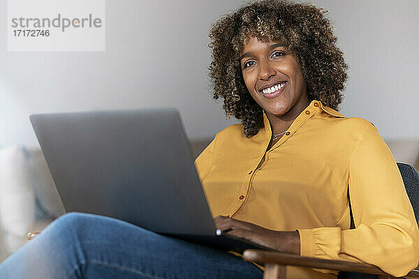 Mittlere erwachsene Frau mit Laptop  die wegschaut  während sie zu Hause sitzt