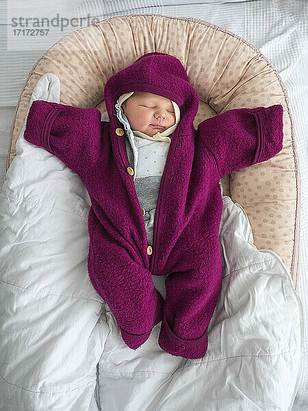 Niedliche Baby-Mädchen in warmer Kleidung schlafen auf dem Bett zu Hause