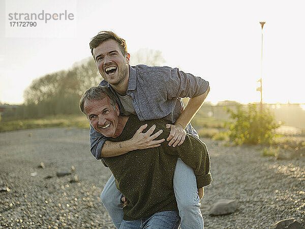 Cheerful father carrying son piggyback at riverbank