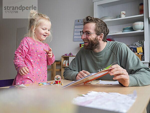 Glücklicher Vater zeigt seiner süßen Tochter ein Buch auf dem Tisch zu Hause
