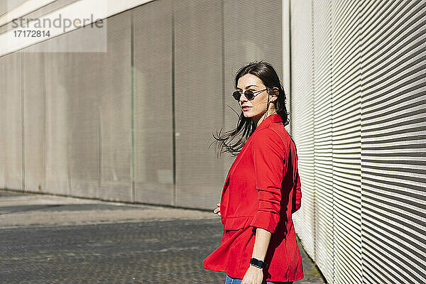 Businesswoman with sunglasses looking away while standing against wall