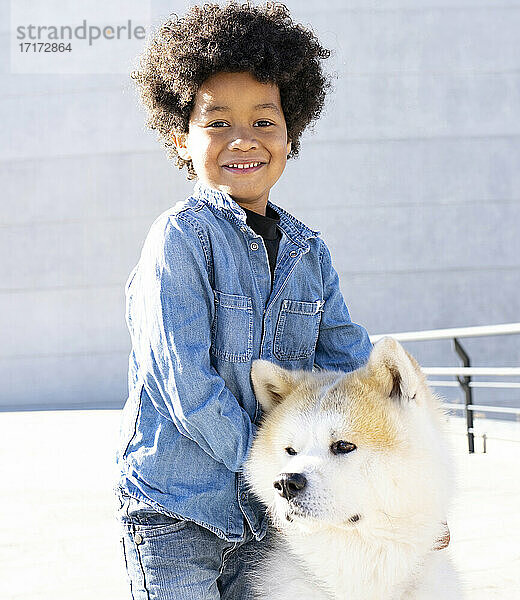 Junge mit Arm um Hund  der lächelnd im Freien steht
