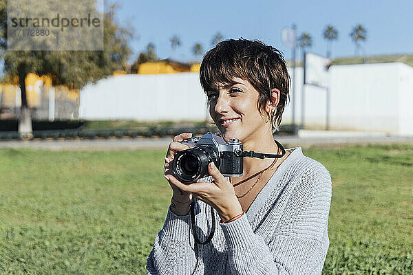 Lächelnde Frau mit analoger Kamera  die im Park sitzt und lächelt