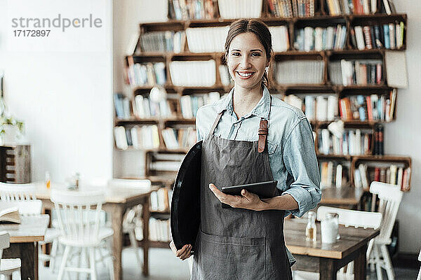 Lächelnde Unternehmerin mit digitalem Tablet und Tablett in einem Café