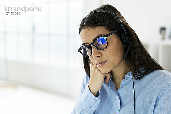 Geschäftsfrau mit Mikrofon-Headset und Brille starrt beim Sitzen im Büro