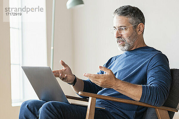 Älterer Geschäftsmann  der zu Hause sitzend einen Videoanruf über seinen Laptop führt