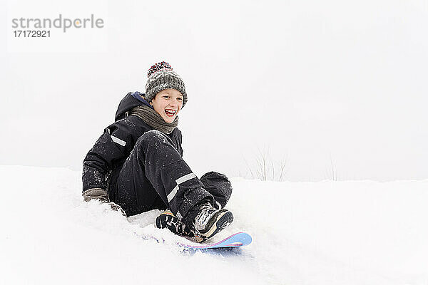Fröhlicher Junge beim Schlittenfahren auf einem schneebedeckten Hügel