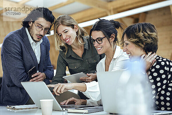 Lächelnde Fachleute  die über einem Laptop im Büro diskutieren