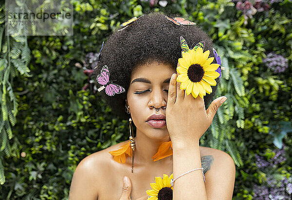 Afro woman covering eye with hand against plant