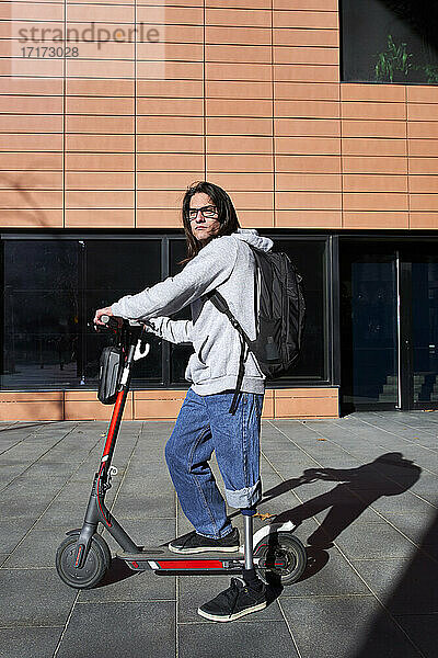 Young disabled man with electric push scooter standing on footpath during sunny day