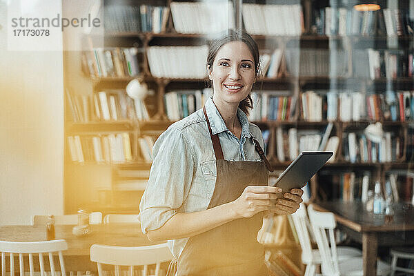 Lächelnde Managerin  die wegschaut  während sie ein digitales Tablet in einem Café hält