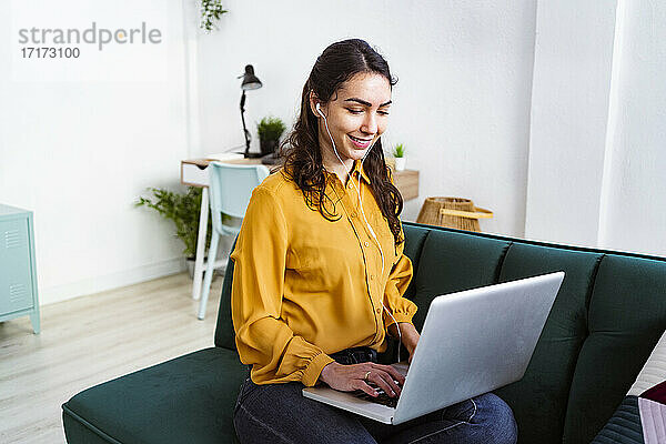 Smiling woman listening music while using laptop sitting at home