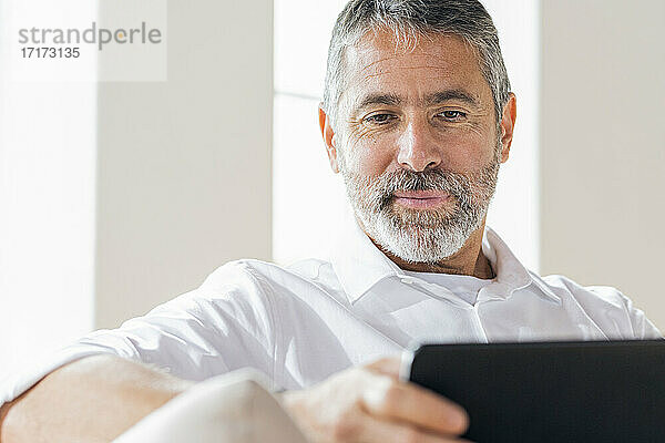 Älterer Geschäftsmann  der zu Hause sitzend ein digitales Tablet benutzt