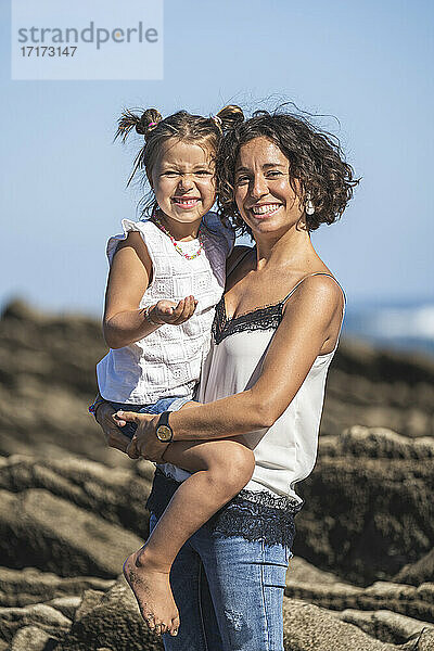Smiling mother holding daughter while standing on flysch during sunny day