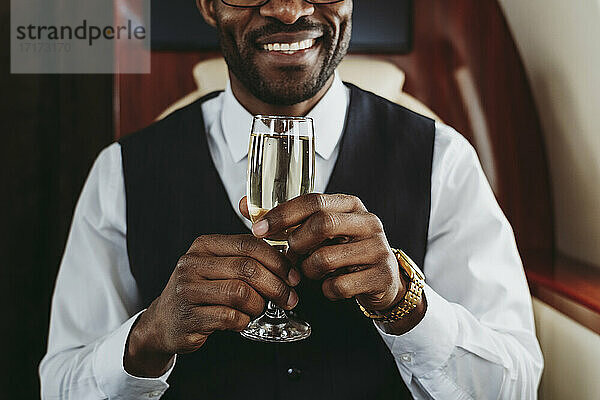 Lächelnder Geschäftsmann mit Champagner in seinem Privatjet