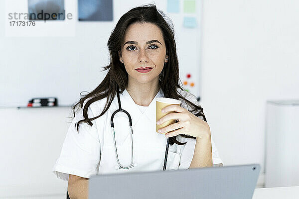 Lächelnde selbstbewusste Ärztin mit Kaffeetasse in der Klinik