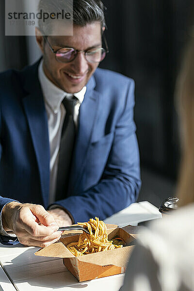 Geschäftsmann isst Essen  während er mit einem Kollegen in der Cafeteria im Büro sitzt