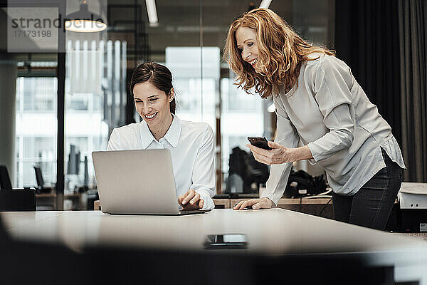 Lächelnde Geschäftsfrau  die an einem Konferenztisch im Sitzungssaal über einem Laptop diskutiert