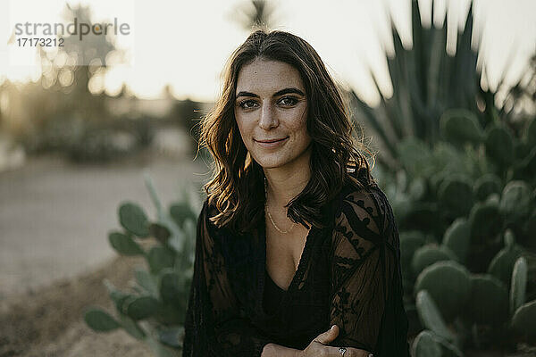 Lächelnde schöne Frau gegen Kaktuspflanzen bei Sonnenuntergang
