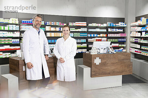 Male with female pharmacist standing against pharmacy checkout in store