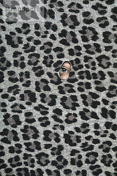 Eye of teenage girl peeking through hole in leopard print pattern