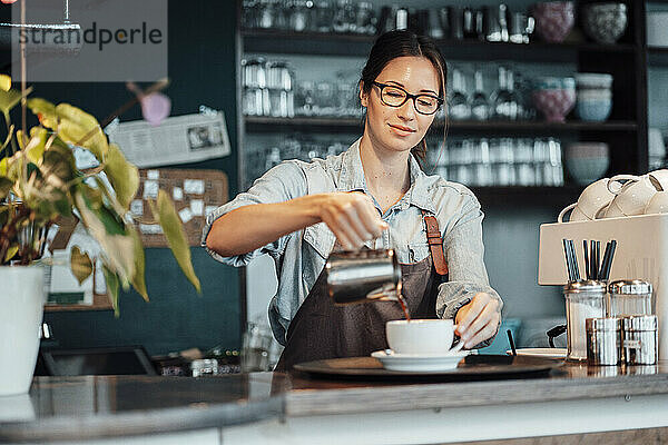 Weibliche Besitzerin gießt in einem Café Kaffee in eine Tasse