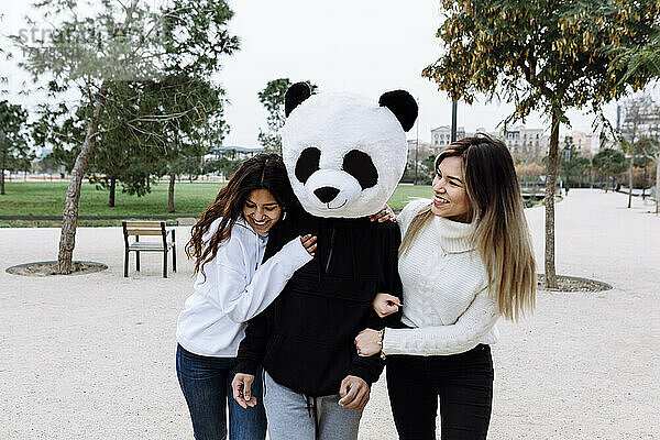 Happy female friends having fun with male friend wearing panda mask at park