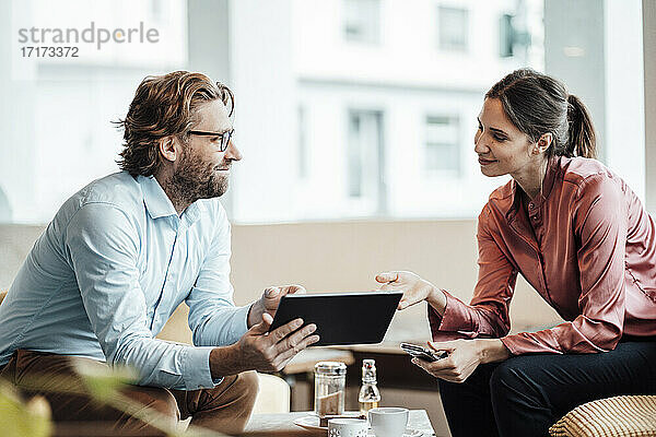 Lächelnde männliche und weibliche Kollegen  die über ein digitales Tablet während eines Treffens in einem Café diskutieren