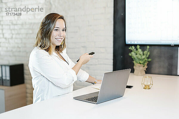 Lächelnde Geschäftsfrau  die eine Projektionsfläche über eine Fernbedienung im Büro bedient