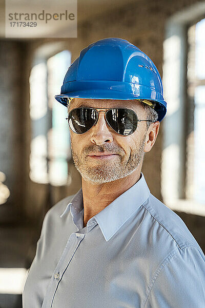 Architekt mit Sonnenbrille und Schutzhelm  lächelnd auf einer Baustelle