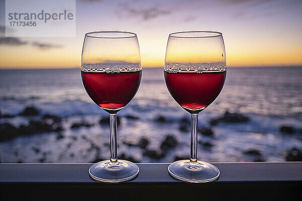 Zwei Gläser Rotwein mit Meer bei Sonnenuntergang im Hintergrund