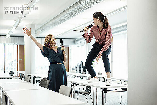 Fröhliche Kolleginnen singen am Mikrofon am Konferenztisch  während sie eine Pause im Büro machen