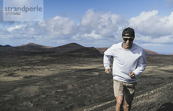 Fröhlicher männlicher Tourist  der während der Ferien auf dem Vulkan El Cuervo läuft  Lanzarote  Spanien