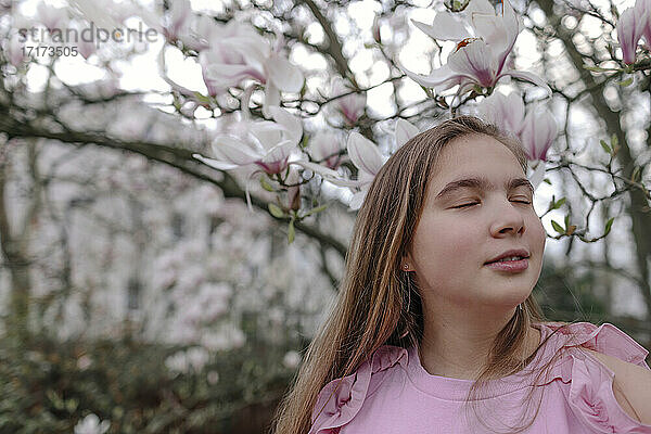 Teenage girl with eyes closed against magnolia tree in park