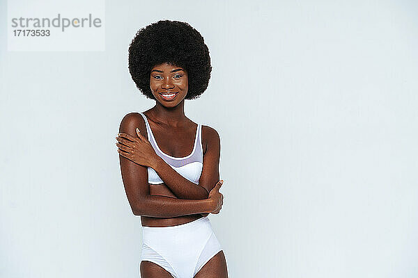 Skinny weibliches Modell trägt Dessous mit gekreuzten Armen stehen gegen weißen Hintergrund
