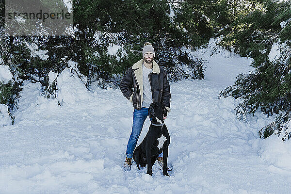 Mann mit Hund in verschneitem Land vor Bäumen stehend