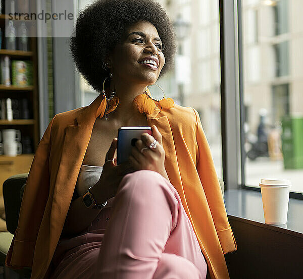 Smiling woman with smart phone looking out of window in cafe