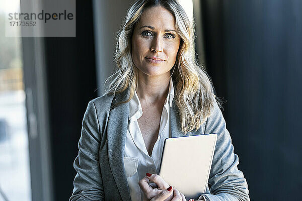 Confident businesswoman holding digital tablet while standing at office